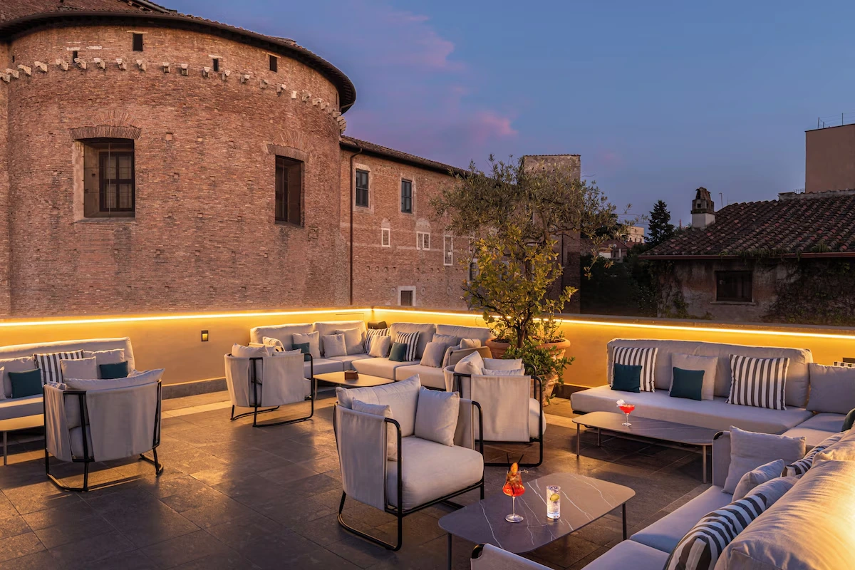 Room Mate Collection Mia rooftop lounge at dusk with comfortable seating and historic Rome architecture