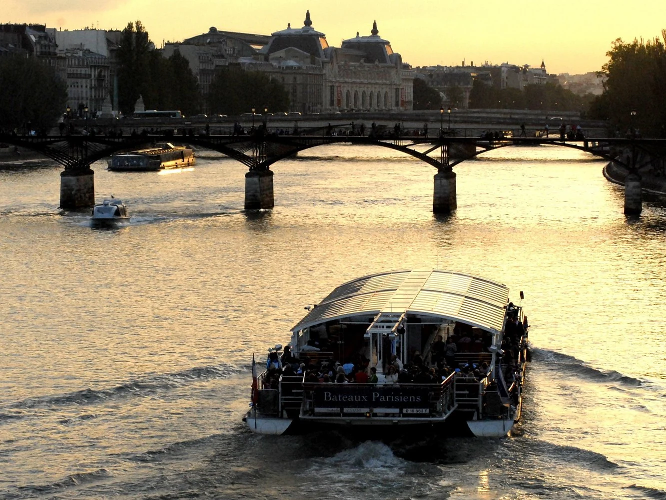 Sightseeing boat cruising on the Seine at sunset beneath a Paris bridge